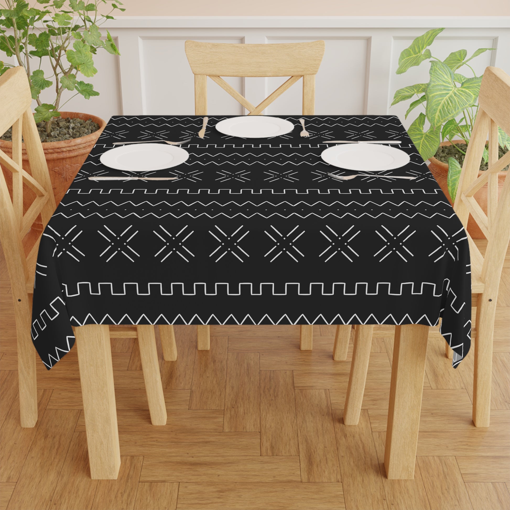 A black and white mudcloth print tablecloth on a table with plates and chairs, featuring a geometric pattern.