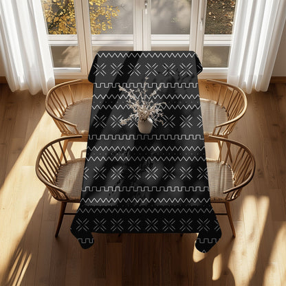 A black and white mudcloth print tablecloth on a table with plates and chairs, featuring a geometric pattern.