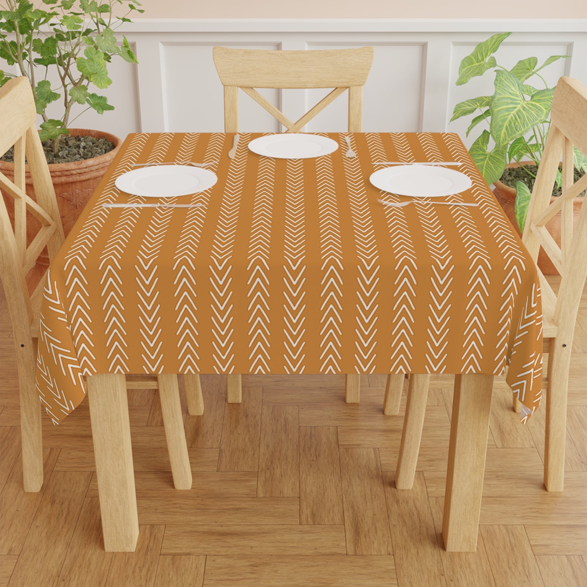 An orange tablecloth with a white geometric pattern laid out on a table with plates and chairs.