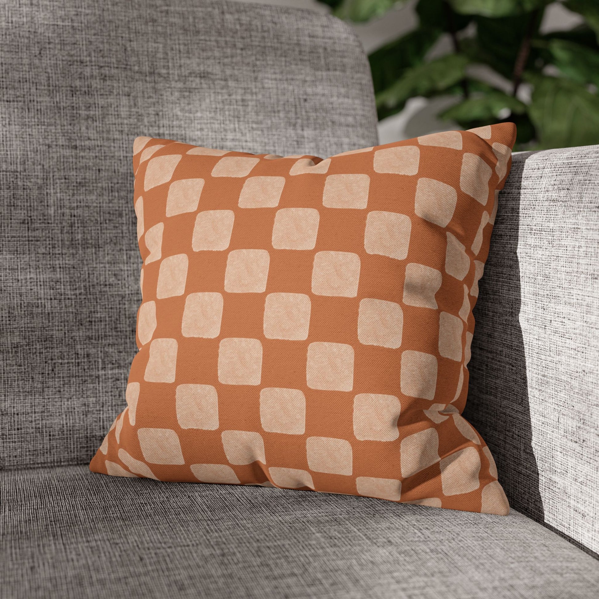 Checkered pillow on a gray sofa with a blurred green plant background