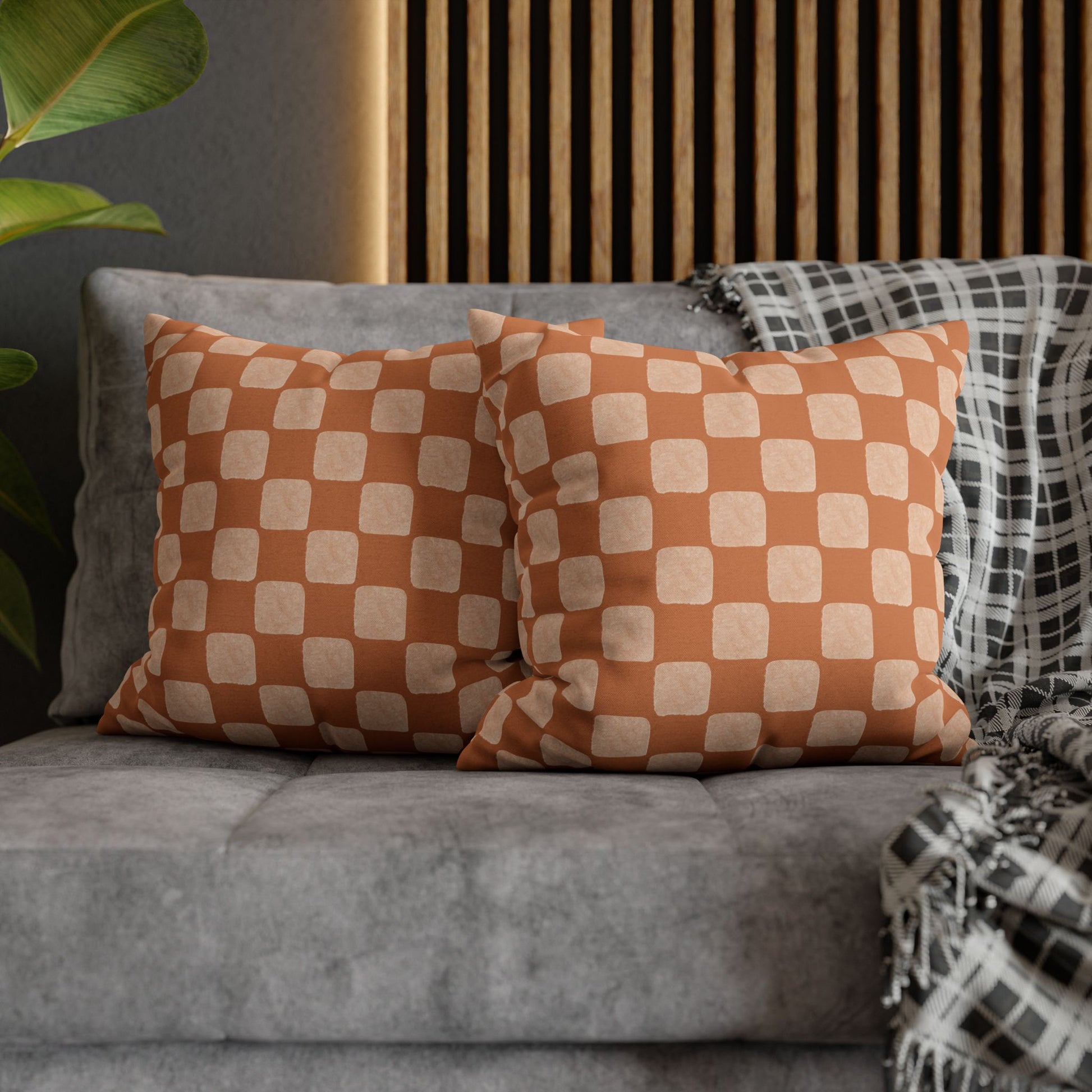 Checkered orange and white pillows on a gray sofa with a wooden headboard in the background.