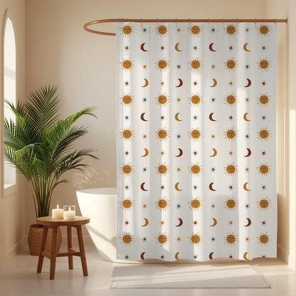 A white shower curtain with a repeating pattern of gold suns, brown crescent moons, and small blue stars, hanging in a bright bathroom next to a potted palm plant and a small wooden stool.