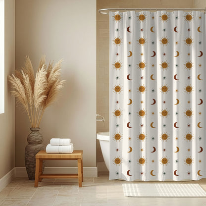 A white shower curtain with a repeating pattern of gold suns, brown and gray crescent moons, and stars, hanging in a bathroom next to a wooden bench with folded towels and a vase of pampas grass.