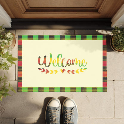 Doormat with 'Welcome' text on a checkered Kente cloth border, placed on a wooden floor.