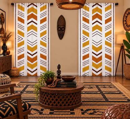 A styled living room with two tall patterned curtains featuring vertical chevron and arrow motifs in white, mustard yellow, ochre, and brown. The room includes warm lighting, a woven rug, a round wooden coffee table, decorative masks, and plants.