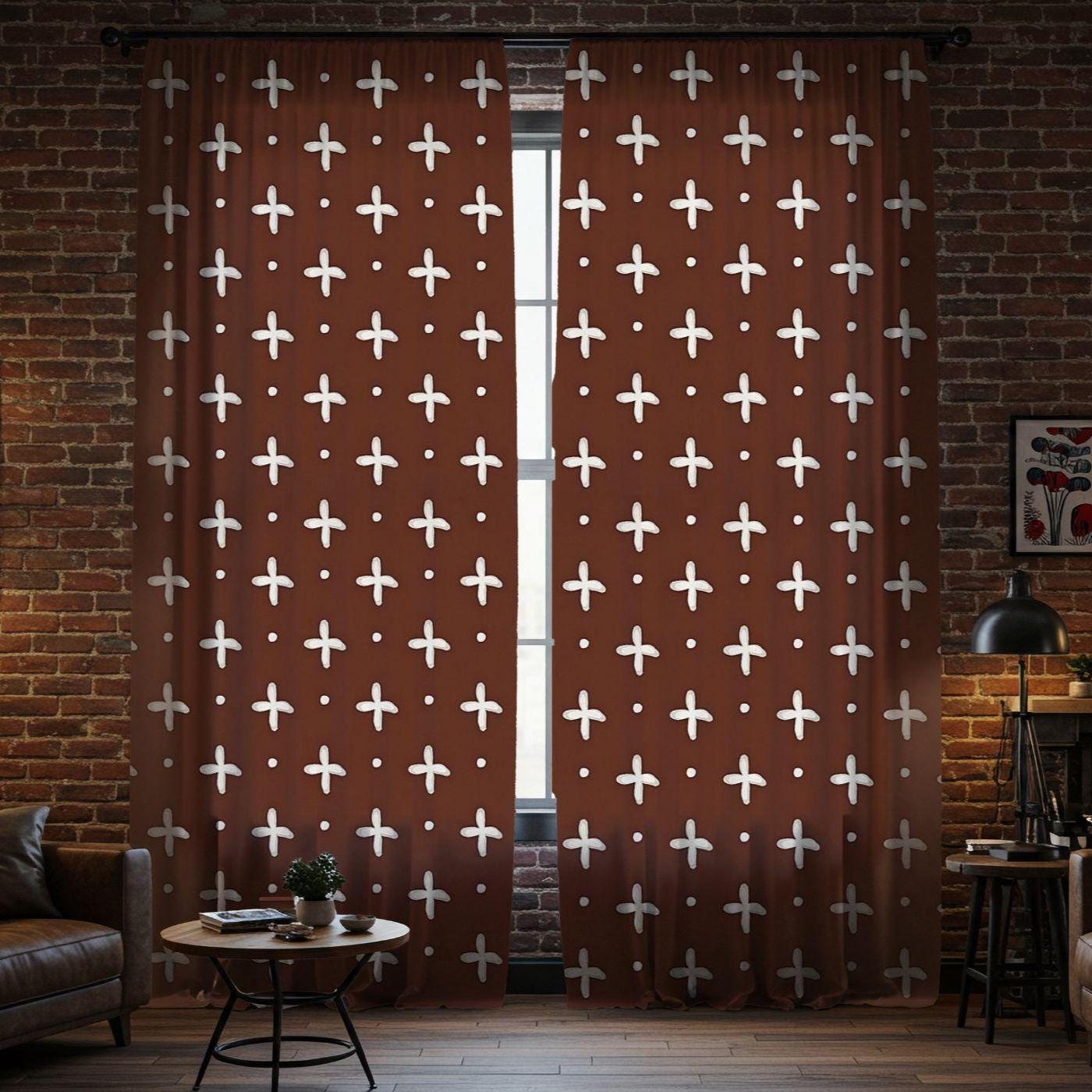 Brown curtains with white cross patterns in a room with a brick wall and furniture.