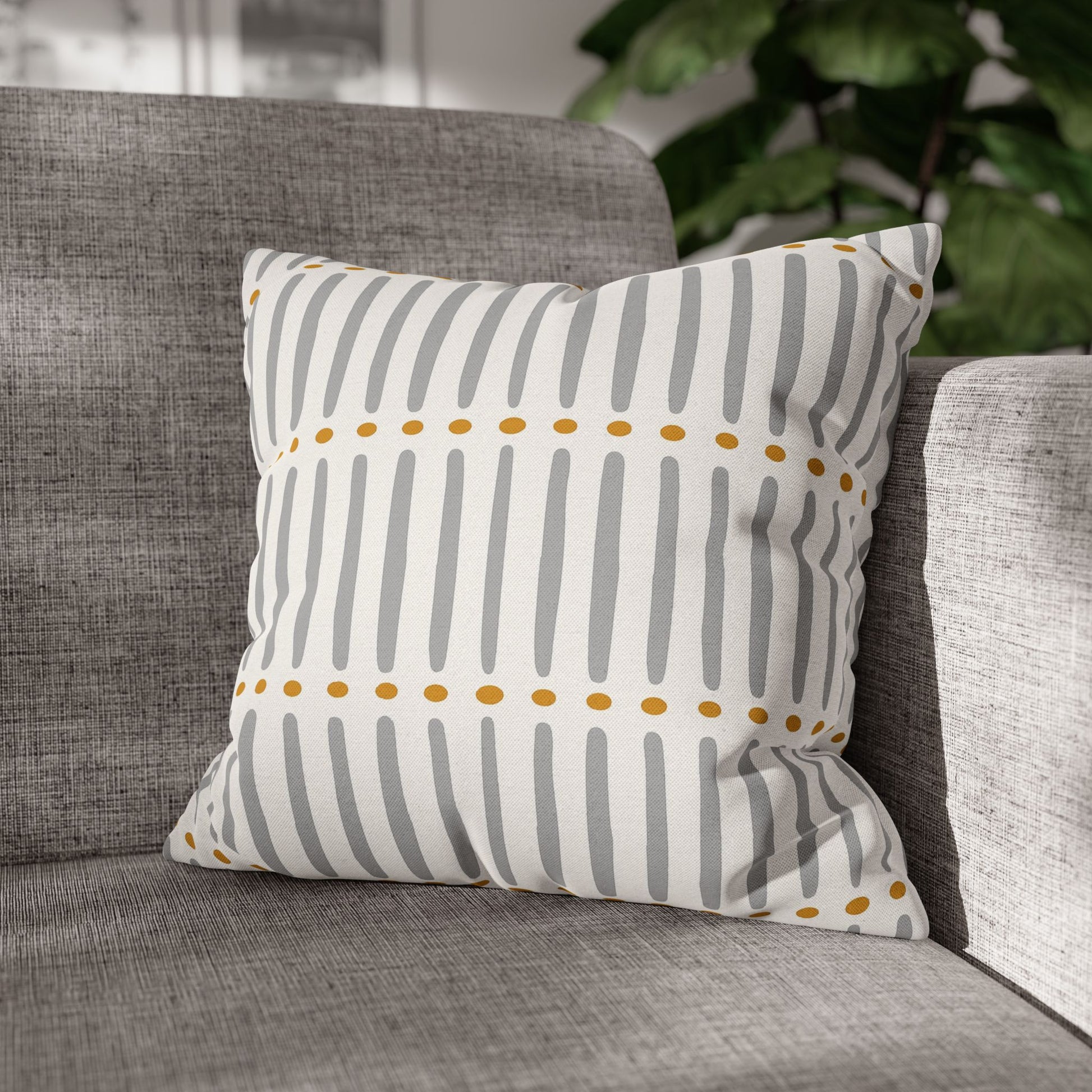 Decorative mudcloth  pillow with gray stripes and yellow dots on a gray sofa.