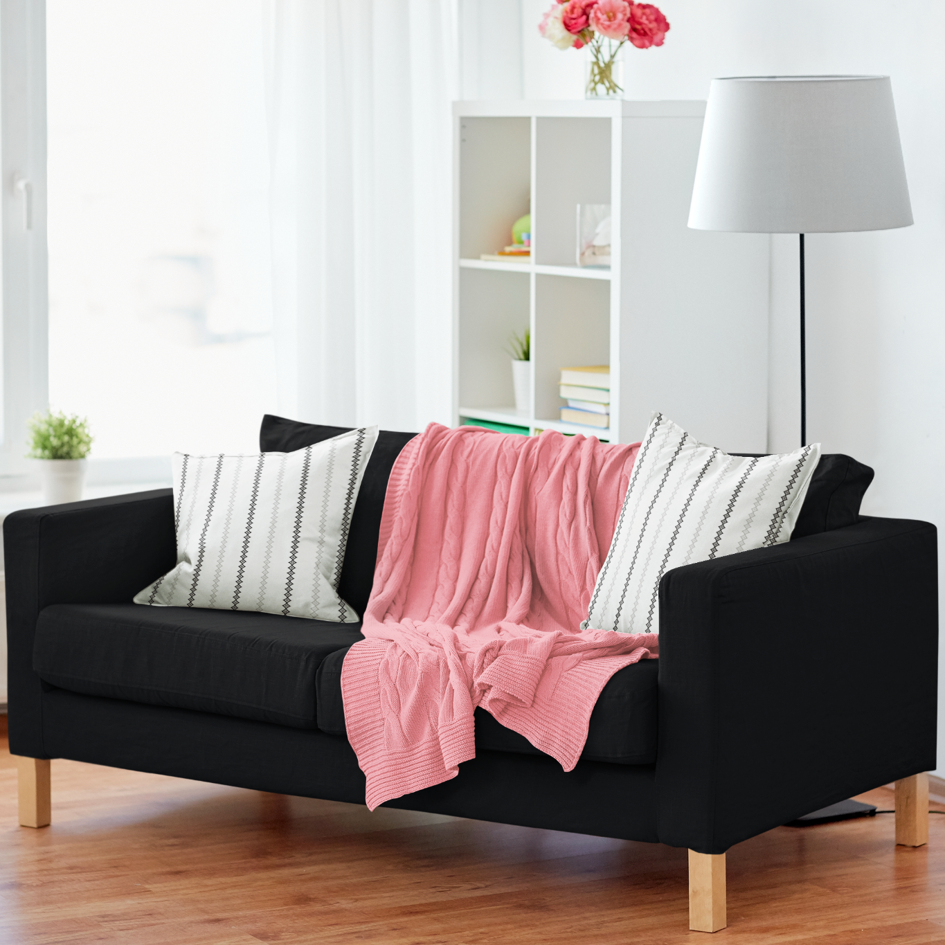 Black sofa with a pink blanket and striped cushions in a bright living room.