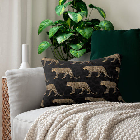 A lumbar pillow with a black leopard print design placed on a sofa, next to a green cushion and a wicker chair with a large green leafy plant in the background.
