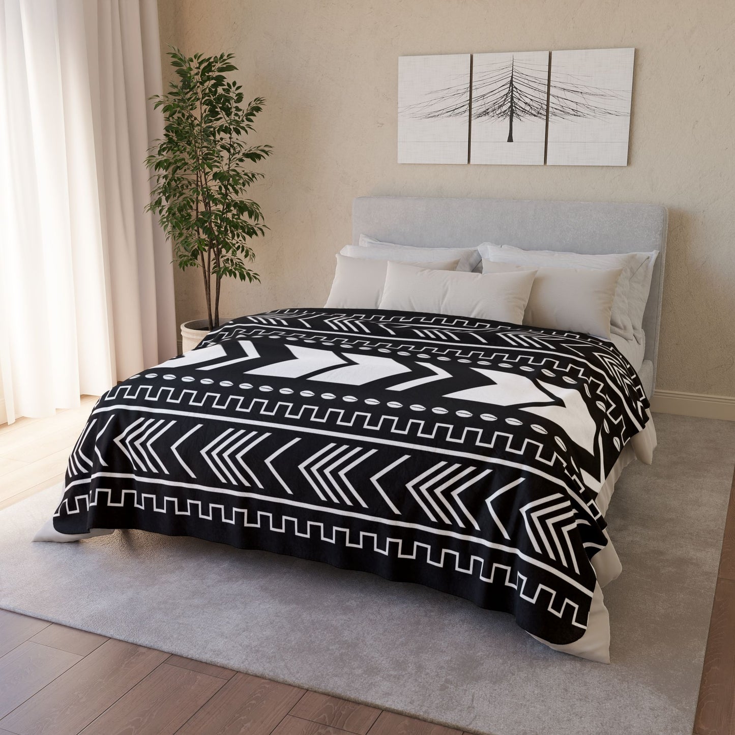 Bedroom with a bed covered by a black and white patterned duvet, light-colored walls, and a plant.