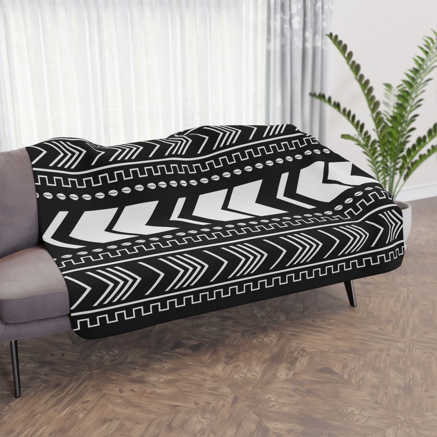 Black and white patterned throw blanket draped over a sofa in a room with curtains and a plant.
