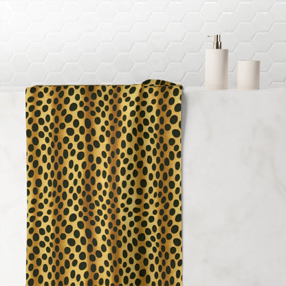A towel with a retro jungle pattern, featuring a vibrant combination of yellow and black dots, hanging on a white marble bathroom wall next to a candle holder and a roll of toilet paper.
