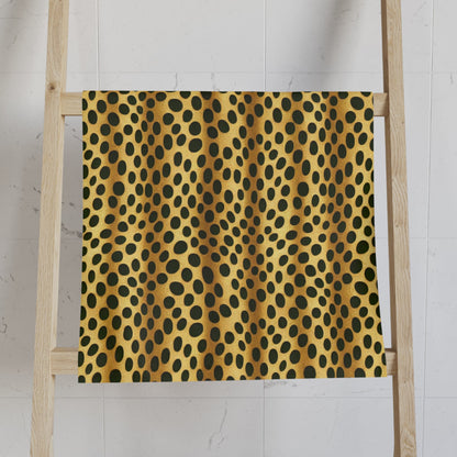 A towel with a retro jungle pattern, featuring a vibrant combination of yellow and black dots, hanging on a white marble bathroom wall next to a candle holder and a roll of toilet paper.