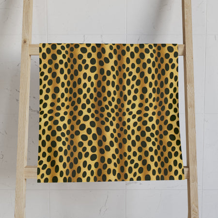 A towel with a retro jungle pattern, featuring a vibrant combination of yellow and black dots, hanging on a white marble bathroom wall next to a candle holder and a roll of toilet paper.
