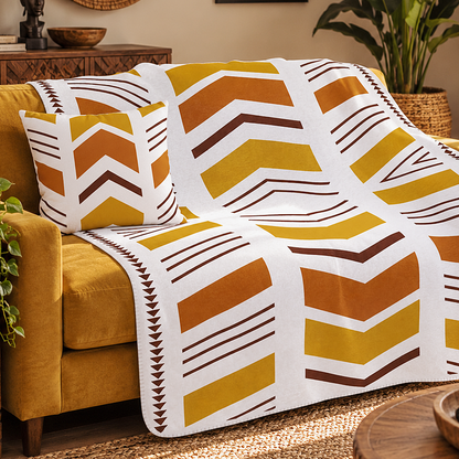 A patterned throw blanket and matching pillow cover draped over a mustard yellow armchair in a styled living room setting.